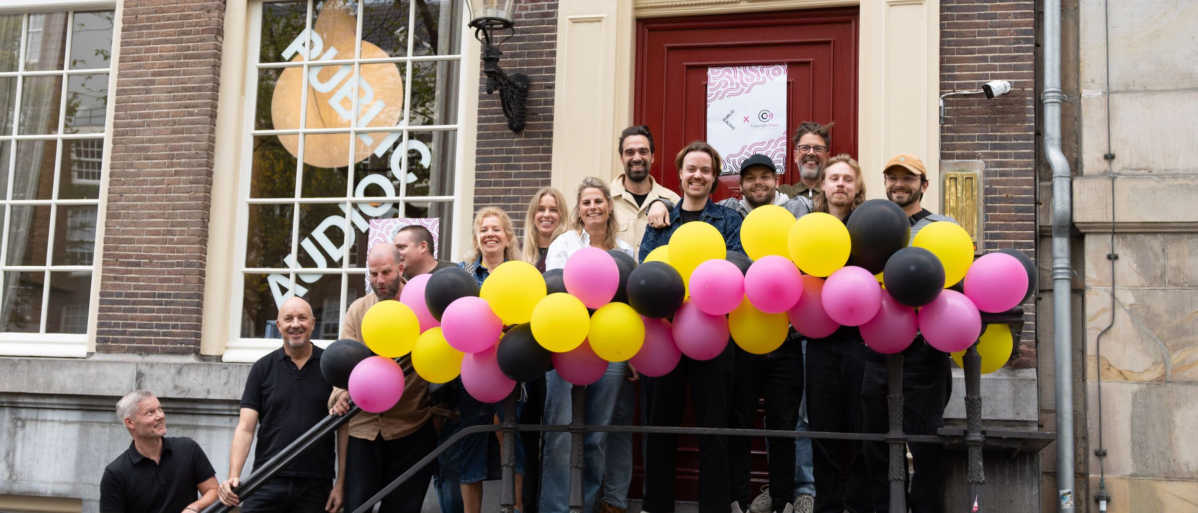 The Public Audio × CPI writers camp group on the steps, with pink, yellow and black balloons